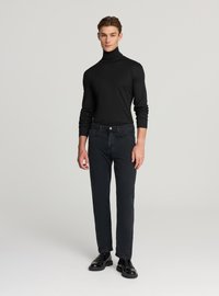 Maglione nero a collo alto abbinato a jeans scuri. Silhouette aderente, tessuto liscio con una sottile lucentezza. Scarpe nere e lucidate.