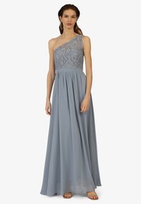 Ein-Shoulder-Abendkleid in Hellblau mit einem Spitzenoberteil, einem fließenden Chiffonrock und dezenten Falten an der Taille. Sandalen in neutralen Tönen.