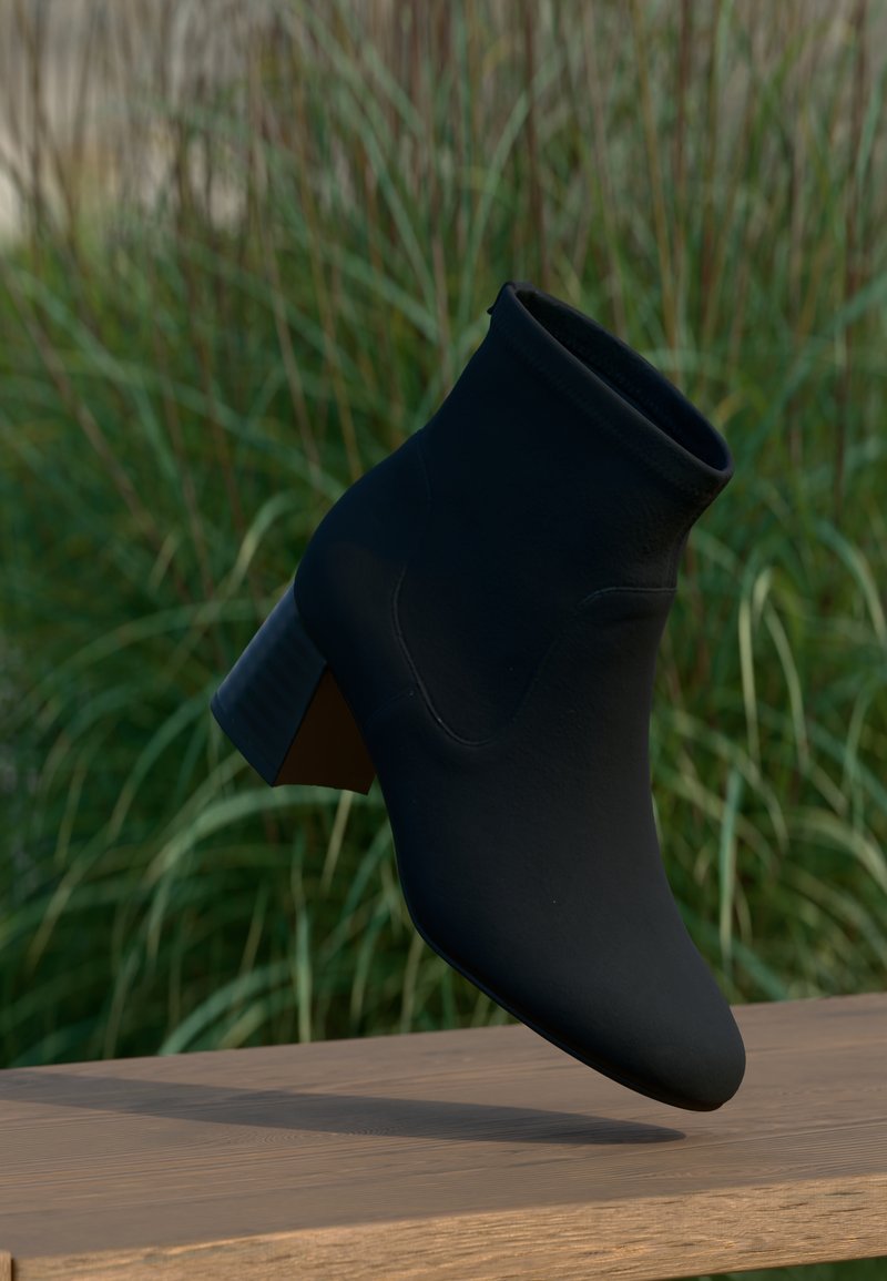 Černé kotníkové boty s elegantním designem, měkkým materiálem, špičatou špičkou a blokovým podpatkem. Jemné švy. Umístěno na zelené trávě.