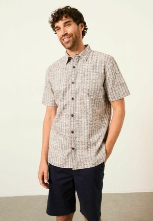 Kurzärmliges Hemd mit durchgehender Knopfleiste in hellen Farben und floralem Muster. Mit Kragen, Knopfverschluss und Brusttasche; kombiniert mit dunklen Shorts.