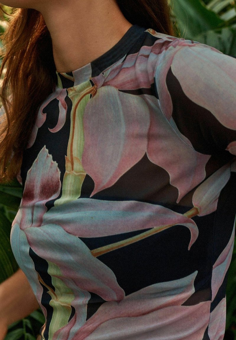 Hedvábný top s květinovým potiskem, který obsahuje velké růžové orchideje na černém pozadí. Je vyroben ze strečového materiálu, má vysoký límec a krátké rukávy.