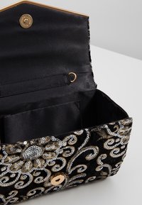 Černá sametová kabelka s vyšíváním ve zlaté a stříbrné barvě, květinovými vzory a hladkým saténovým interiérem. Disponuje zlatým zacvakávacím uzávěrem a vnitřní kapsou.