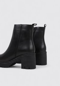Bottines noires en cuir lisse, avec un bout arrondi, une fermeture éclair latérale et un design de talon épais à rainures.
