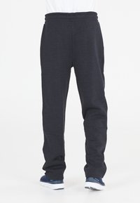 Mörkgrå sweatpants med elastisk midja, åtsittande ben, mjukt material och lös passform, i kombination med marinblå sportskor.