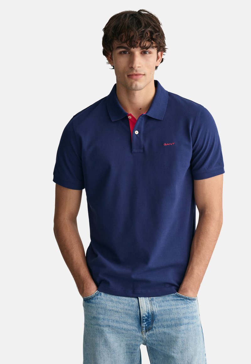 Navyblaue Poloshirt mit rotem Innenkragen, kurzen Ärmeln und einem GANT-Logo auf der Brust; aus glattem Baumwollstoff gefertigt.