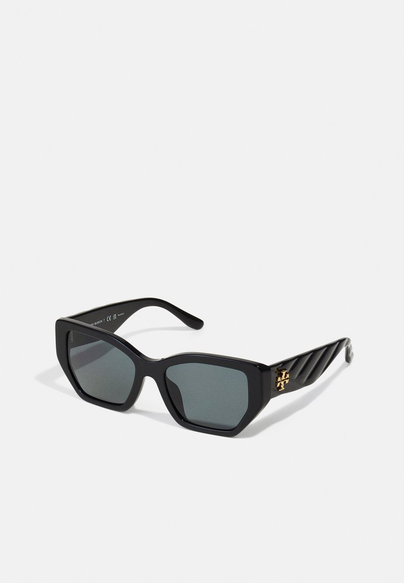 Black sunglasses with a chunky frame, gray lenses, and a gold logo accent on the side. The temples feature a ribbed texture design.