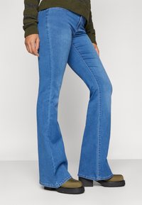 Jeans blu a palazzo con design a vita media, caratterizzati da una superficie di denim liscia e un leggero dettaglio di cucitura, abbinati a stivali platform verdi.