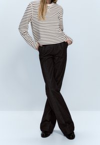 Maglietta a maniche lunghe a righe crema e marrone scuro abbinata a pantaloni larghi e scuri. I pantaloni hanno tasche frontali e una texture liscia.