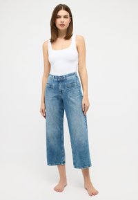 Blue denim wide-leg jeans with a mid-rise waist, two front pockets, and a slightly faded finish. Paired with a fitted white tank top.