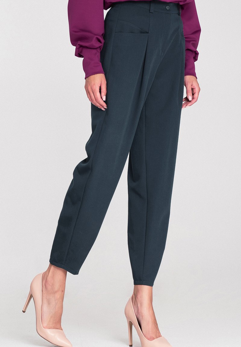 Ciemnozielone, dopasowane spodnie o luźnym kroju, z frontowymi fałdami i tylnią kieszenią, w połączeniu z nagimi szpilkami. Gładka tekstura materiału.
