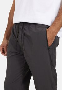 Czarne lekkie spodnie z elastycznym pasem, sznurkiem i siateczkowymi bocznymi kieszeniami. Materiał ma gładką teksturę i subtelny blask.