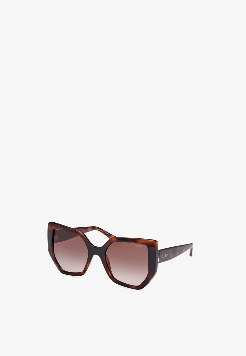 Lunettes de soleil surdimensionnées en écaille de tortue avec une monture géométrique, verres dégradés marron, et logo de la marque en relief sur les branches.