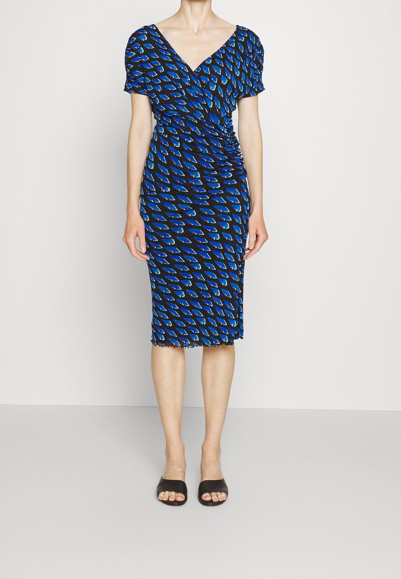 Niebiesko-czarna sukienka do kolan z dekoltem w serek, krótkimi bufkowatymi rękawami, marszczonym bokiem i geometrycznym wzorem. Czarne wsuwane buty.