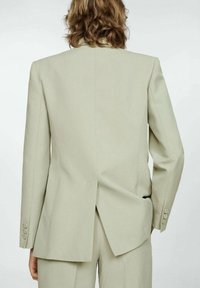 Beige přizpůsobený blazer vyrobený z hladkého materiálu, s jedním rozparkem na zadní straně a manžetami na knoflíky. Design je minimalistický a strukturovaný.