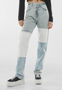 Vaqueros de patchwork en denim con paneles en azul claro y blanco, cintura alta, pierna recta y dobladillo deshilachado. Combinados con zapatillas de plataforma negras.