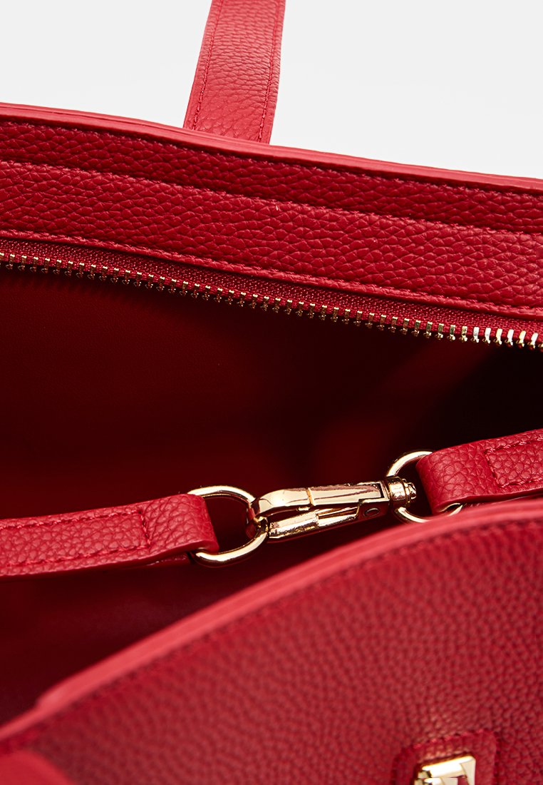 Intérieur d'un sac en cuir rouge texturé avec une fermeture éclair dorée, doté d'une sangle et d'un clip assortis, et d'une doublure lisse pour un accès facile.