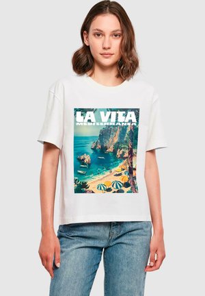 T-shirt en coton blanc avec un graphique coloré de plage méditerranéenne, accompagné du texte "LA VITA MEDITERRANEA" et des tons océaniques bleu-vert.