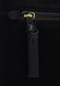 Černý zamšový zipový pouzdro se zlatými prvky. Obsahuje texturovanou černou koženou poutko a hladké švy podél okrajů.