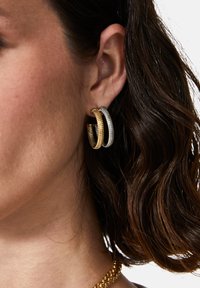 Guld- och silverörhängen med en texturerad design. Örhängena har en skiktad struktur som framhäver kontrasterande metalliska ytor.