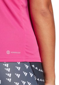Camiseta deportiva rosa con una textura suave, que presenta el logo "AEROREADY" en blanco. Combinada con leggings estampados en gris y blanco.