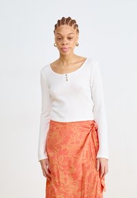 White long-sleeve ribbed top with scoop neckline and three buttons. Paired with an orange floral-patterned wrap skirt. Smooth texture.