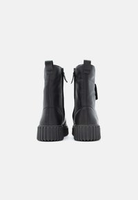 Svarte skinnankelsko med bakre glidelåser, teksturerte gummisåler og tabakenter. Minimalistisk design med en glatt overflate og solid konstruksjon.