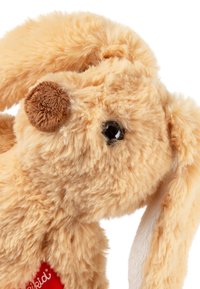 Stuffed rabbit in light tan fur, with a brown nose, black eyes, and long ears. Features a red tag on its side with white text.