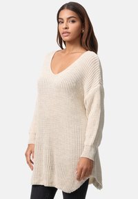 Strickpullover in Elfenbein mit V-Ausschnitt, oversized Passform, gerippter Textur und langen Ärmeln. Seitliche Schlitze am Saum für zusätzlichen Komfort.