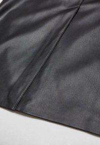 Gros plan sur un tissu en cuir noir avec une texture de grain visible et une couture diagonale sur un fond clair.