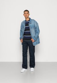Denim jacket, striped navy and white t-shirt, and navy trousers. White sneakers. Smooth texture, casual design, front pockets on jacket.