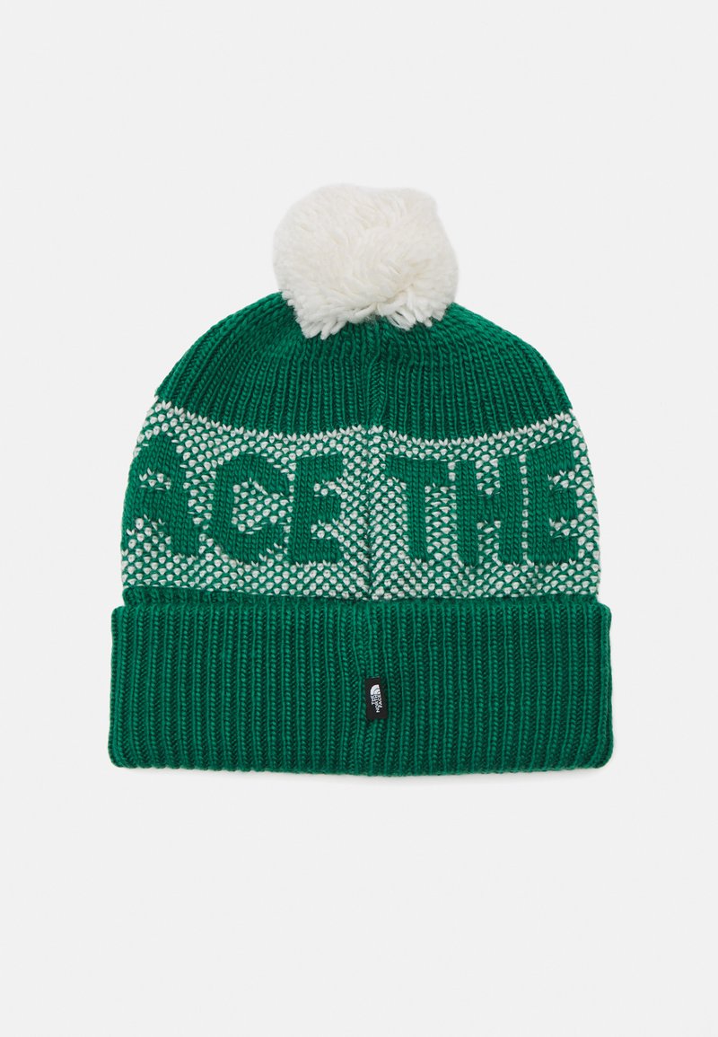 Zaļš adīts cepure ar baltu adījumu, uz kura rakstīts "ACE THE", un balts pom-poms augšpusē. Cepurei ir ribota josta un zīmola etiķete.