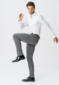 Grå strækbukser med slim fit og subtil tekstur, parret med en hvid skjorte med knapper og sorte dressko.