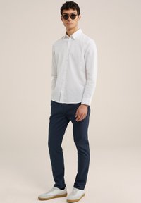 Witte overhemd met knopen, marineblauwe broek en witte sneakers. Het overhemd heeft een kraag en knopen; de broek is op maat gemaakt met een gladde textuur.