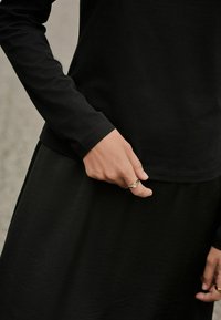 Black long-sleeve top paired with a flowing black skirt, featuring a smooth texture and a hand with a ring resting on the fabric.