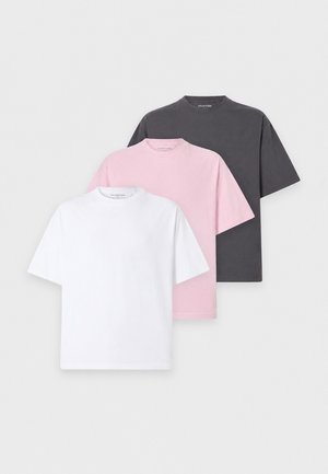 En mand og en kvinde står side om side iført hvide t-shirts, lyse og mørke vidde jeans og hvide sneakers mod en ensfarvet hvid baggrund.