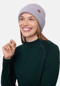 Gray knitted beanie with a ribbed pattern and a small brown leather tag. Model wears a dark green turtleneck. Simple, casual design.
