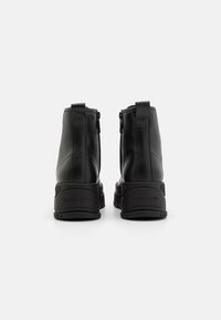 Bottines en cuir noir avec une finition lisse, dotées d'une fermeture éclair à l'arrière et d'une semelle en caoutchouc robuste embossée avec "TOMMY JEANS."