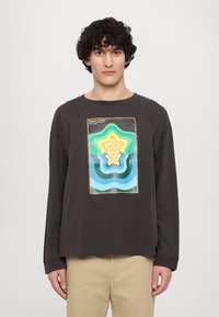 Čierne tričko s dlhým rukávom so farebnou grafikou sústredených hviezdnych tvarov v zelenej, žltej a modrej farbe. Mäkká látka s voľným strihom.