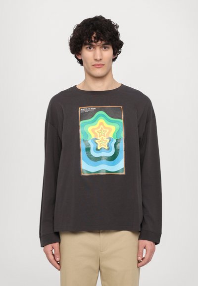 T-shirt noir à manches longues présentant un graphique coloré de formes d'étoiles concentriques en vert, jaune et bleu. Tissu doux avec une coupe décontractée.