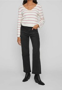 Biały sweter dziergany z czerwonymi poziomymi paskami, zestawiony z czarnymi dzwonami z denimu z wysokim stanem oraz czarnymi botkami na obcasie.