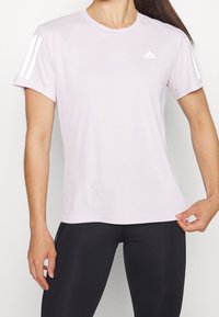 Ljusrosa kortärmad träningsskjorta i fuktavvisande tyg, med vita tre-stripes accent på ärmarna och en Adidas-logotyp.