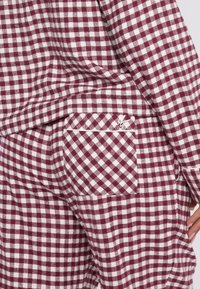 Burgundy ja valge ruuduline lounge-segment, mis sisaldab tekstuurset kangast. Tuntud tasku detail kontrastse äärega.