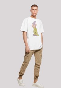 Hvit t-skjorte med grafikk av en tegneseriefigur, kombinert med beige cargo-bukser og hvite sneakers. Laget av bomull, avslappet passform.