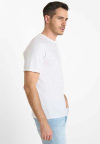 Witte t-shirt met korte mouwen van lichtgewicht stof, voorzien van een ronde halslijn en knoopdetail, gecombineerd met lichtblauwe jeans.