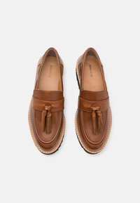 Mocassins en cuir marron avec des pampilles sur le dessus, semelles cousues et semelles intérieures rembourrées, vus de dessus sur un fond neutre.