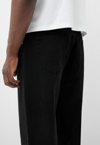 Černé džínové kalhoty s rovnými nohavicemi, středně vysokým pasem a zadními kapsami. Tkanina má hladkou strukturu s minimálními detaily.