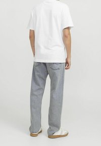 Camiseta blanca de manga corta combinada con jeans de mezclilla azul claro, con un corte relajado. Los jeans tienen un sutil desgastado y bolsillos traseros.