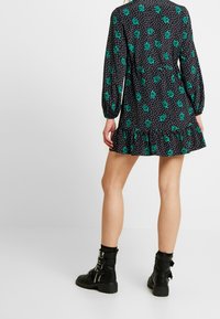 Vestito nero con motivo floreale verde e pois bianchi, caratterizzato da maniche lunghe e orlo arricciato. Abbinato a stivaletti neri.