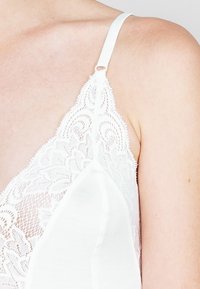 Witte kant bralette met intricates bloemmotieven, verstelbare bandjes en een gladde onderlaag voor comfort en ondersteuning.