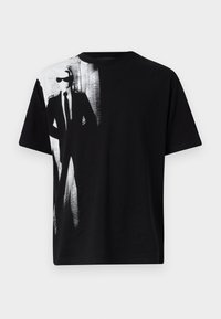 Črna bombažna majica z velikim belim grafičnim prikazom oblečenega figura na levi strani. Okrugli izrez z kratkimi rokavi, gladka tekstura.